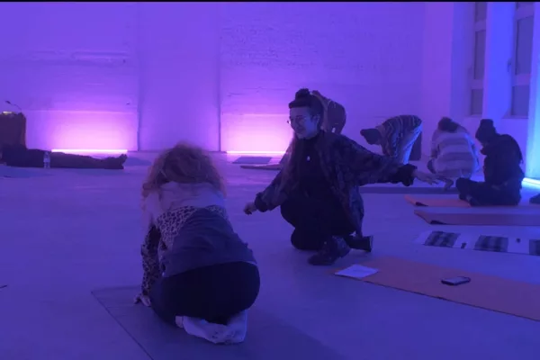 cours de yoga bruxelles dans une pièce éclairée par des néons bleu et rose deux silhouettes accroupies qui parlent sur des tapis de yoga bruxelles Saint-gilles