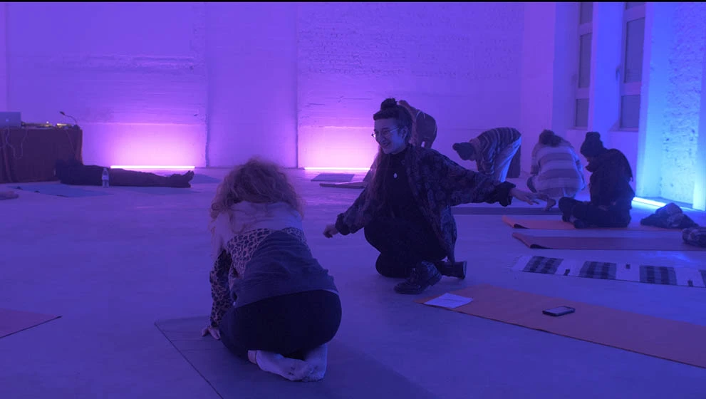 cours de yoga bruxelles dans une pièce éclairée par des néons bleu et rose deux silhouettes accroupies qui parlent sur des tapis de yoga bruxelles Saint-gilles